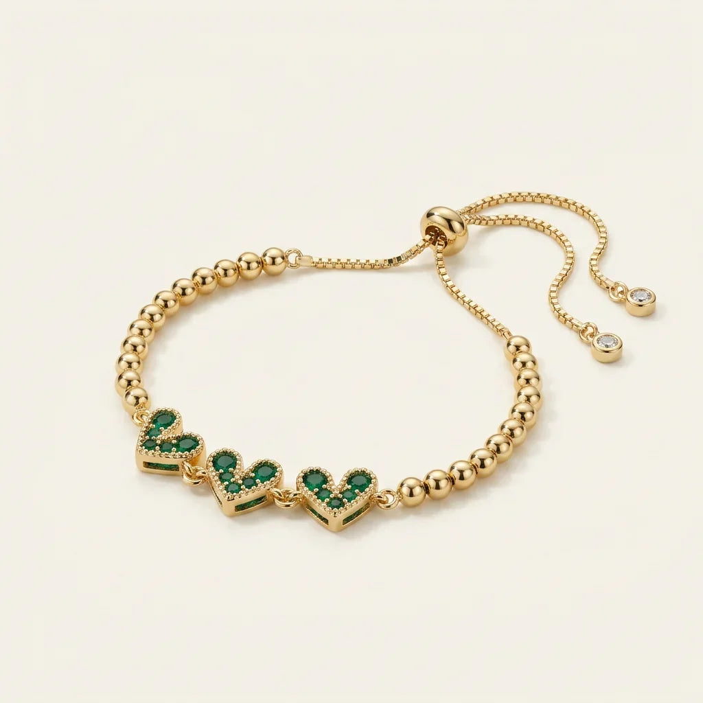 Gold beaded bracelet with three pave green cubic zirconia hearts and an adjustable slider clasp.